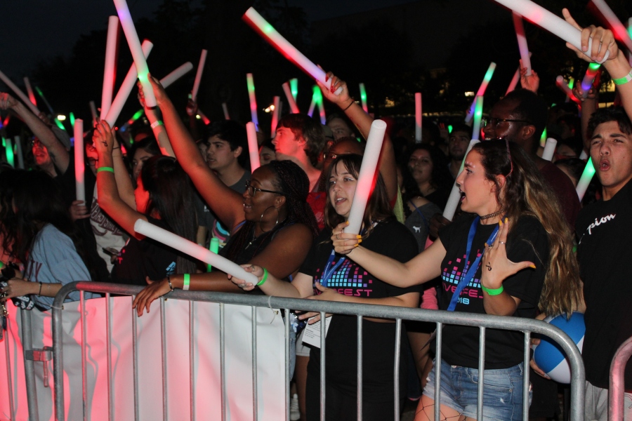 Many students enjoying the show at night. They are all holding foam batons with red, blue, and green lights inside.