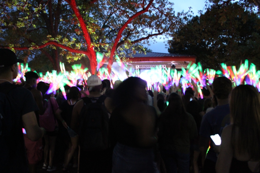 Hundreds of students stand in front of the stage at Sewell Park with light-up foam batons.